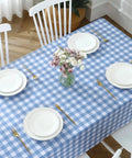 Buffalo Gingham Waterproof Vinyl Tablecloth Heavy Duty Wipeable Checkered Table Cover Outdoor Patio Picnic Camping 54 X 78 Inches Light Blue Spillproof PVC Protector with plates and flowers on top.
