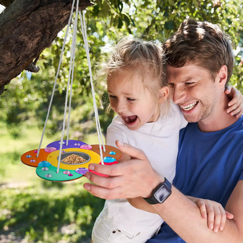 Father and daughter hanging a painted feeder from the Two Pack Diy Wooden Bird Feeder Craft Kits For Kids Outdoor Fun.