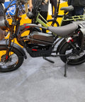 Black electric bike with 20 inch fat tires, displayed at an exhibition, featuring saddle bags and upright handlebars.