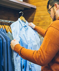 Man organizing shirts with 300 Pack Plastic White Clothes Hanger End Caps With Rounded Corners No Glue Needed Protective Covers For Iron Wire Hangers Quick Install And Closet Organization A Must Have Space Saving Storage Solution