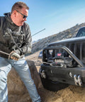 Man using Warn Vro Evo 10 Standard Duty 12V DC Electric Winch With Steel Rope on a Jeep during off-road recovery.