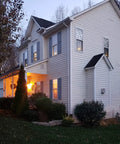 Evening view of cozy home with glowing windows using 12 Pack Battery Operated Taper Candles With Remote, Warm White Flicker.