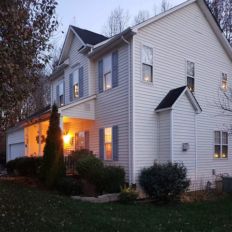 Evening view of cozy home with glowing windows using 12 Pack Battery Operated Taper Candles With Remote, Warm White Flicker.