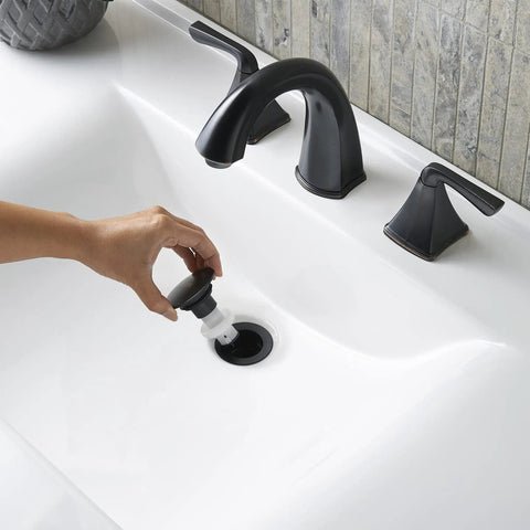 Hand demonstrating Push and Seal drain on Selia 8 Inch Widespread Bathroom Sink Faucet Two Handle 3 Hole Deck Mount in Tuscan Bronze Finish