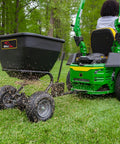 Tow Behind Broadcast Spreader With Universal Hitch 175 Lb Capacity Durable Poly Hopper attached to a mower spreading seeds on grass