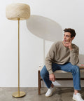 Rowan Brass Floor Lamp With Unique Thread Shade beside seated man in casual outfit, highlighting modern living room setting.
