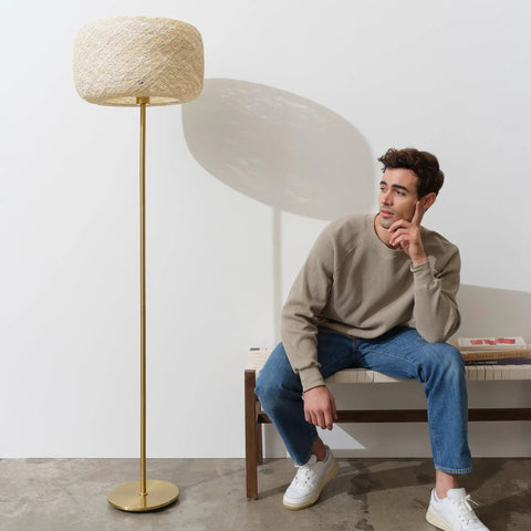 Rowan Brass Floor Lamp With Unique Thread Shade beside seated man in casual outfit, highlighting modern living room setting.