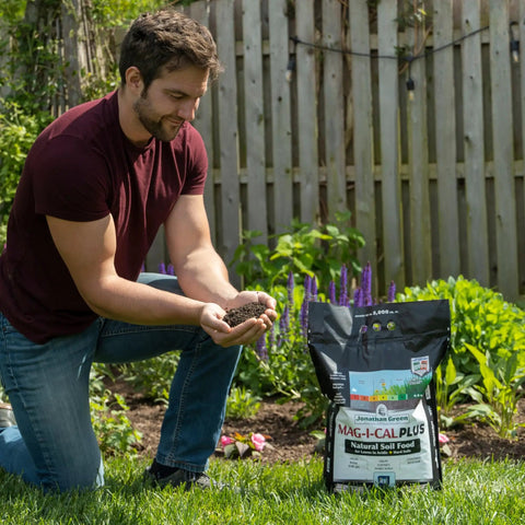 Man kneeling in garden with Mag-I-Cal Plus Soil Booster For Lawns, Raises pH In Acidic And Hard Soils, 18 lb bag on grass.