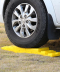 Top Shelf RV Leveling Blocks 12 Pack Stackable Jack Pads under tire on grass, durable yellow polypropylene for camper support.