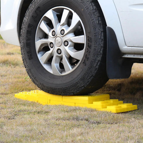 Top Shelf RV Leveling Blocks 12 Pack Stackable Jack Pads under tire on grass, durable yellow polypropylene for camper support.