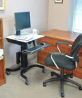 Smooth Roll Single Monitor Sit Stand Desk With Zero Effort Height Lift And Heavy Duty Caster Wheels For Vesa Monitors Up To Twenty Four Inches in an office setup.