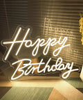 Birthday Neon Sign Led Flex Transparent Acrylic Letter Board Backlight Neon Light For Wall Decor And Party Setup 3D Personalized Neon Signs For Home Bar Room Decor 23.6 x 15.75 Inches Lit Colorful Glow For Party Vibes showing 'Happy Birthday' letters on a floor near a vase.