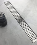 36 Inch Offset Linear Shower Drain With Side Outlet And Quadrato Grate Cover Brushed 304 Stainless Steel in a bathroom setting.