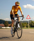 Cyclist on road bike wearing helmet; background of clear sky and bike path sign.
