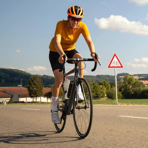 Cyclist on road bike wearing helmet; background of clear sky and bike path sign.
