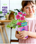 Child holding decorated pot with pink zinnias, part of the Paint And Plant Stoneware Flower Garden Kit For Kids 6 To 12, Paint Pots.