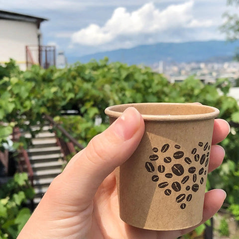4 Oz Espresso Cups 100 Pack Kraft Disposable Paper Cups For Home Office Or Party held outdoors with coffee beans design
