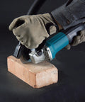 Powerful 4-1/2 Inch Angle Grinder With Kick Butt Strength cutting through a brick with dust control.