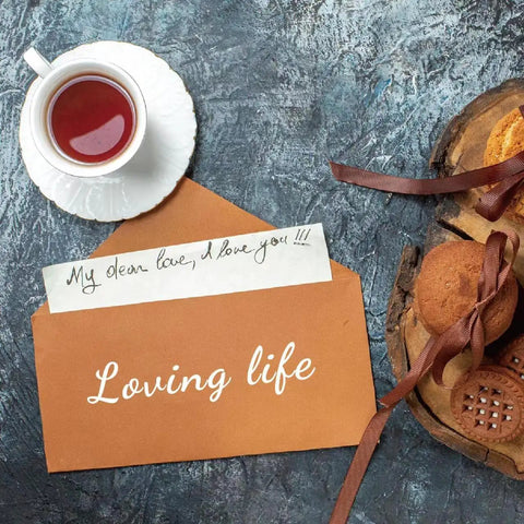 A cup of tea, brown envelope with 'Loving life', and cookies on a textured surface.