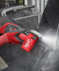 Milwaukee 12V cordless cut-off tool, bare tool in red, cutting a metal panel with guard, held by gloved hands