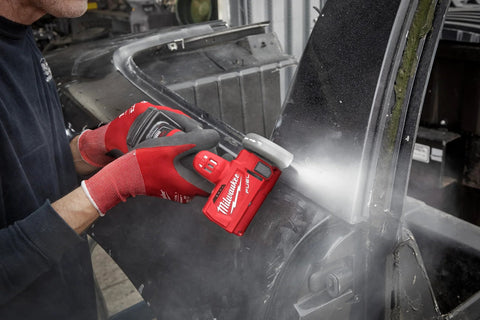 Milwaukee 12V cordless cut-off tool, bare tool in red, cutting a metal panel with guard, held by gloved hands