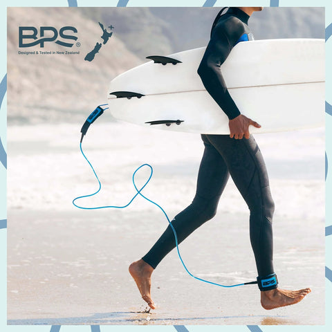 Surfer walking on beach carrying board with Storm 8mm Surfboard Leash 8 Ft Premium Leg Rope attached, Koru Dark Blue