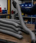 Heavy Duty Universal Absorbent Socks 12 Plus Pack Spill Containment Tubes Industrial Grade, gray tubes stacked on workbench.