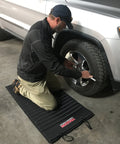 Man kneeling on VersaMat Roll Up Workhorse High Density Foam Utility Mat Black for Garage while working on a car tire