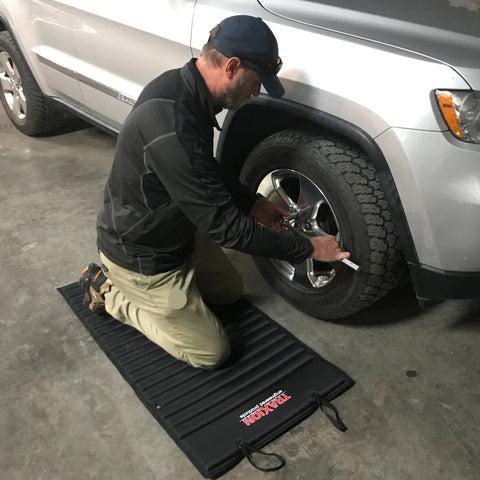 Man kneeling on VersaMat Roll Up Workhorse High Density Foam Utility Mat Black for Garage while working on a car tire