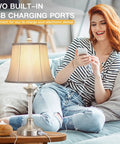 Set Of 2 Silver Touch-Activated Bedside Lamps With Dual USB Ports, woman using 3-way dimmable lamp, modern bedroom setting