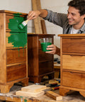 Man applying No Sweat Heavy Duty Green Wood Stain And Deck Sealant For Exterior Fences Porch Boards And Patio Decks Zero VOC Matte Finish on wooden drawer.