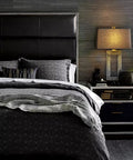Luxury bedroom interior with textured gray bed linens, modern lamp on a nightstand, black leather headboard, and decorative accents.