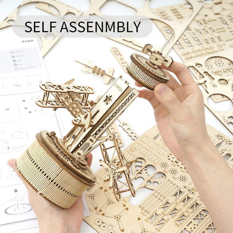 Hands assembling 3D Wooden Puzzle Mechanical Music Box Aircraft Model Kit For DIY Builders, parts and gears visible.