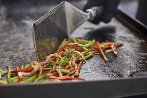 Spatula flipping sliced peppers on a griddle from the Griddle Essential 5 Piece Tool Set With Spatula Flexible Spatula Scraper And Two Squeeze Bottles For Breakfast Pancakes Burgers And More Game Changer Easy Cooking And Cleanup On The Griddle.