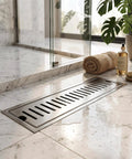 Oreilet Linear Shower Drain 12 Inch Floor Drain with Hair Catcher installed on marble bathroom floor with a towel and shower gel.