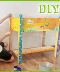 Child decorating raised wood planter box on legs with storage shelf for vegetables flowers and herbs, DIY natural finish.