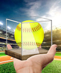 Clear Acrylic Softball Display Case With Wood Base For One Ball held in hand with ball inside on a baseball field background