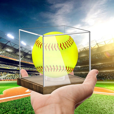 Clear Acrylic Softball Display Case With Wood Base For One Ball held in hand with ball inside on a baseball field background
