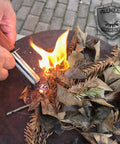 Person using All Weather Survival Fire Starter with Magnesium Ferro Rod and Euro Ferrocerium to ignite dried leaves.