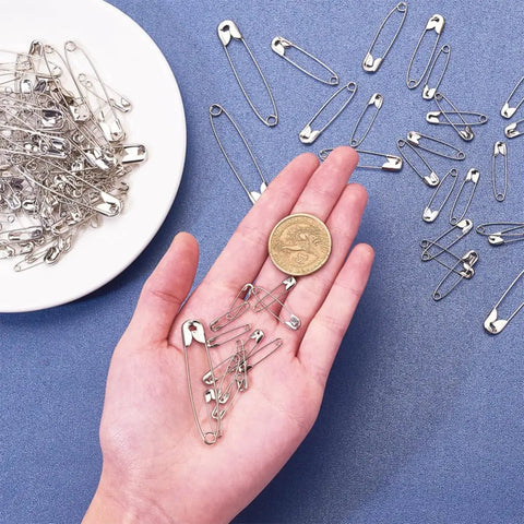450 Pack Real Deal Iron Safety Clasp Pins For Crafting And Tailoring in hand with a coin for size reference.