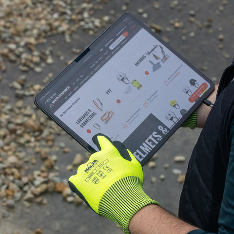 Person wearing heavy duty industrial work gloves with ANSI cut level A5 protection using a touchscreen device outdoors.