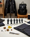 Six Black Zipper Sliders Replacement Kit for Quick Fixes on a table with sewing tools and black fabric, jacket, and backpack.