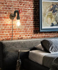 Water Pipe Wall Light Fixture Vintage Steampunk Sconce with plug-in cord next to a bed against a brick wall showcasing industrial style.