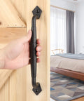 Rustic 12 Inch Barn Door Handle Heavy Duty Pull For DIY Sliding Doors Gates Sheds And Garages Round Solid Metal With Matte Black Finish Built To Stand Up To Everyday Use And Easy Mounting installed on wooden door with hand.