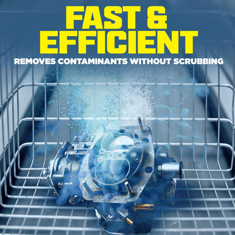 Front view: automotive carburetor submerged in blue ultrasonic cleaner solution inside a metal wire basket