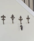 Built Like A Tank Cast Iron Wall Mount Key Hooks For Entryway And Garage Featuring Classic Fleur De Lis Charm Dark Brown, set of four on wall.