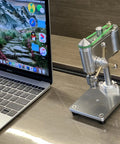 Kickass Mini Drill Press And Compact Benchtop Drilling Station For High Precision Woodworking and Epoxy Casting Featuring Variable Speed Control and a Rock Solid 0.3 To 4 Mm Chuck Setup For Snappy Hobby Projects next to a laptop.