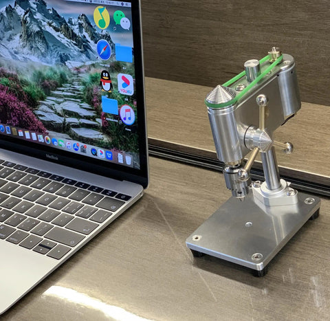 Kickass Mini Drill Press And Compact Benchtop Drilling Station For High Precision Woodworking and Epoxy Casting Featuring Variable Speed Control and a Rock Solid 0.3 To 4 Mm Chuck Setup For Snappy Hobby Projects next to a laptop.