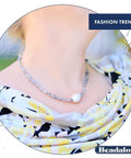 Woman wearing a beaded necklace with a large pearl pendant, against a floral patterned dress in an outdoor setting.