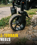 Close-up of all-terrain wheel on Foldable Wagon Cart With Drop Down Tailgate For Groceries And Gear, on sandy and rocky ground.